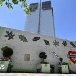 A woman and girl look up at Grenfell Tower from in front of a wall covered in written tributes