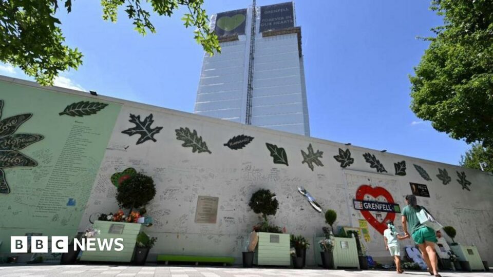 A woman and girl look up at Grenfell Tower from in front of a wall covered in written tributes